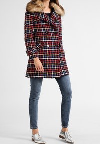 Červený, námořnický a bílý kockovaný kabát s límcem z umělé kožešiny, dvouřadovým zapínáním a bočními kapsami. V kombinaci s džínami a stříbrnými botami.