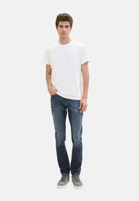 Camiseta de algodón blanca, jeans de mezclilla azules, zapatillas ligeras de color gris. Ajuste casual, con un diseño sencillo y sin patrones o adornos visibles.