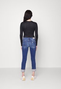 Camiseta negra de manga larga combinada con jeans azul ajustados. Los jeans tienen un lavado desgastado y puños enrollados, complementados por zapatillas blancas.