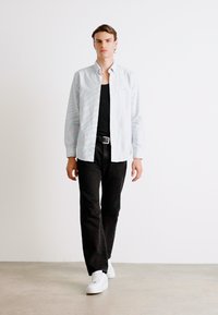 Camisa de manga larga a rayas azules claras combinada con una camiseta sin mangas negra, pantalones negros y zapatillas blancas; tela suave, corte ajustado.