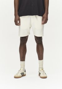 Vita shorts med ett texturerat mönster, bärs med krämfärgade strumpor och beigea sportskor med svarta ränder. Stylat med en svart topp.