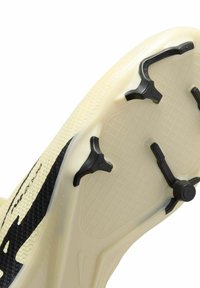 Schoenzool in crème met zwarte hardware. Voorzien van een textuur oppervlak en opvallende studs voor grip, ontworpen voor prestaties.