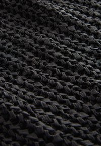 Tessuto nero testurizzato con un intricato motivo intrecciato che presenta sezioni in rilievo e piatte; leggermente elastico con una finitura opaca.