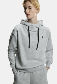Light gray hoodie made from soft material, featuring a kangaroo pocket, black drawstrings, and a small printed logo on the chest.