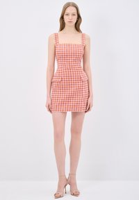 Mini abito a quadri rosa e arancione con scollatura quadrata, corpino aderente, dettagli peplum e spalline larghe. Indossato con tacchi nudi.