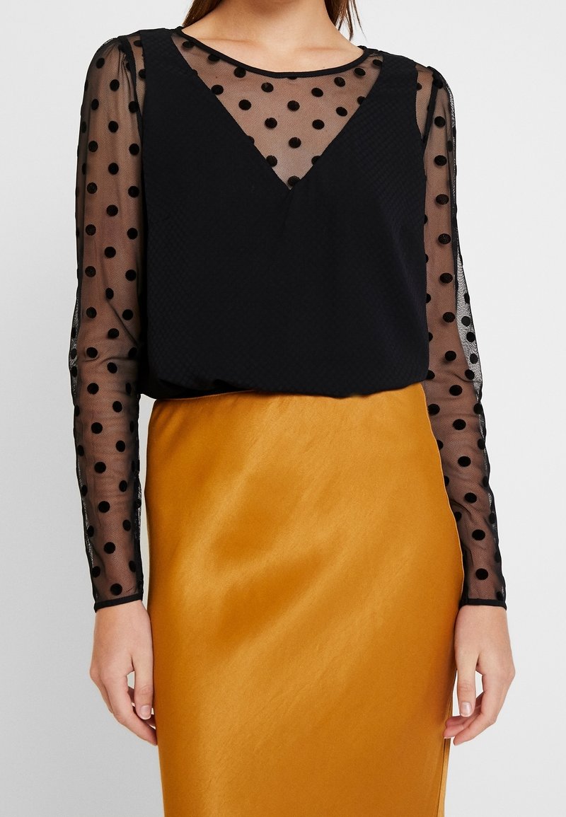 Černé polka dot průhledné dlouhé rukávy s pevným černým tělem, doplněné saténovou sukní ve zlatě žluté barvě. Hladká textura a přiléhavý střih.