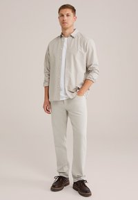 Lichtgrijs overhemd met dunne strepen over een wit T-shirt, gecombineerd met lichtgrijze broeken en donkerbruine schoenen.