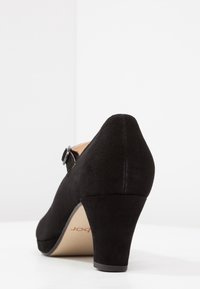 Zapato de tacón alto de ante negro con puntera redondeada, correa al tobillo con hebilla de metal y una plataforma moderada. Textura suave y líneas limpias.