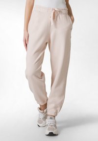Ljusrosa joggingsbyxor i mjukt material, med elastisk midja, dragsko och ankelfållar, tillsammans med vita sneakers.