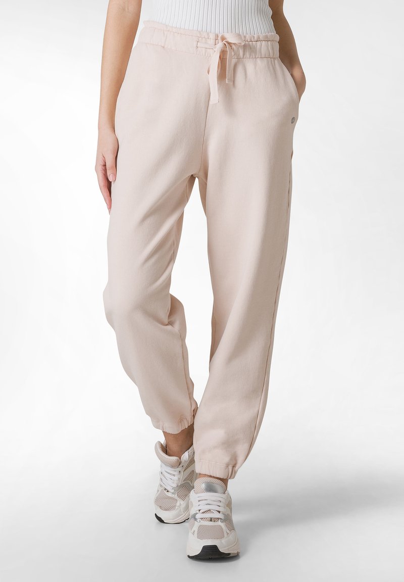 Ljusrosa joggingsbyxor i mjukt material, med elastisk midja, dragsko och ankelfållar, tillsammans med vita sneakers.