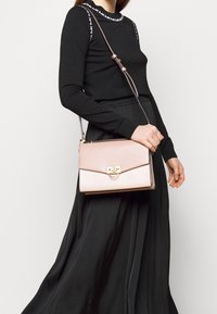 Roségoldene Umhängetasche mit glatter Textur, rechteckiger Form und goldfarbener Verschlussschnalle. Verstellbarer Riemen und schlankes Design.