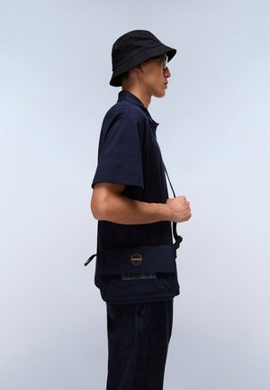 Navy short-sleeve polo shirt paired with a black bucket hat and a navy crossbody bag featuring a circular logo and strap.