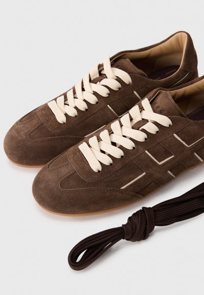 Sneaker in suede marrone con lacci crema in contrasto, caratterizzati da una superficie testurizzata, design minimalista e suola in gomma.