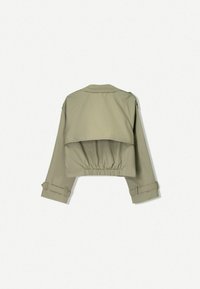 Ingekorte, olijfgroene jas met een uitlopende achterkant, elastische zoom en opgerolde mouwen. Gemaakt van gladde stof zonder zichtbare patronen of accenten.