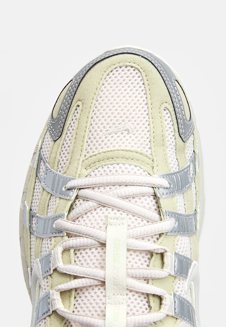 Baskets légères avec un dessus en mesh de couleur crème et vert pastel, ornées d'accents gris, de lacets et d'un branding subtil sur le côté.