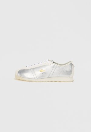 Sneakers din piele argintie cu șireți albi, talpă din cauciuc crem și detalii cu logo auriu. Design elegant cu vârf rotunjit și panouri laterale texturate.