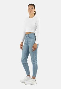 Weißes langärmliges Cropped-Top, hellblaue hoch taillierte Jeans und weiße Sneaker. Schlichtes Design, taillierte Passform, strukturierter Stoff.