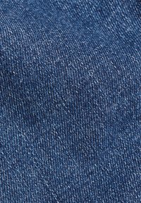 Tela de mezclilla azul que muestra una textura fina acanalada con rayas blancas. El material parece clásico y duradero, con un peso medio.