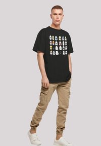 Svart bomull t-skjorte med et grafisk design av forskjellige hjelmmodeller i flere farger. Kombinert med beige cargoskjørt og hvite sneakers.