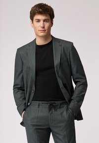 Giacca da completo a quadri grigia con pantaloni abbinati, caratterizzata da una vestibilità su misura, due bottoni e una t-shirt nera sotto.