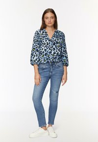Bluzka w niebieski wzór panterki z rękawami o długości trzech kwart i dekoltem w serek; połączona z jasnoniebieskimi, przetartymi rurkami i białymi trampkami.