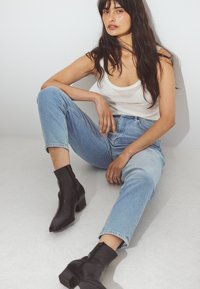 Jean en denim léger taille haute, associé à un débardeur blanc ajusté et des bottines noires à talons carrés. Look contemporain simple.