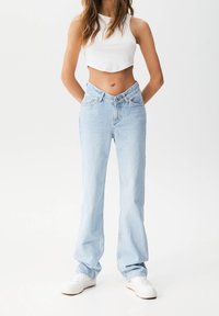 Jean flare en denim bleu clair à taille haute, avec une conception classique à cinq poches et un délavage subtil, associé à des baskets blanches.