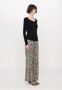 Zwarte longsleeve top gecombineerd met lichtbeige en zwarte broek met slangenprint met wijde pijpen. Sandalen hebben dunne bandjes en een lage hak.