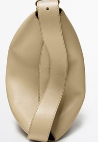 Béžová kožená taška s kulatým, měkkým tvarem a širokým popruhem. Textura je hladká a mírně lesklá, s jemnými detaily prošití.