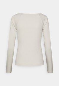 Camisa de manga larga en beige claro, de tejido acanalado. Presenta un escote redondo y una forma ajustada, con hombros sin costuras y una textura suave.