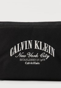 Μαύρο υφασμάτινο πουγκί με λευκό κεντημένο κείμενο "CALVIN KLEIN New York City Established in 1968 Calvin Klein" στο κέντρο.