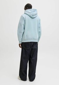 Sudadera con capucha de algodón azul claro, con una capucha grande, combinada con pantalones anchos de mezclilla oscura que tienen bolsillos traseros y costuras visibles.