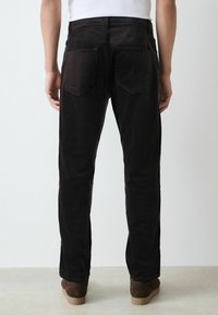 Sorte denimbukser med lige ben, baglommer og en glat overflade, båret med brune sko på en neutral baggrund.