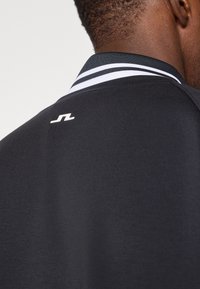 Fekete póló, fehér csíkos bordás gallérral és egy kis logóval a hátán. Puha tapintású, modern szabással.