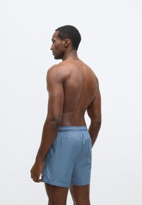 Męskie kąpielówki w jasnoniebieskim kolorze, wykonane z gładkiej, szybko schnącej tkaniny. Posiadają elastyczny pas i boczną kieszeń.