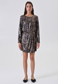 Abito metallizzato con stampa leopardata, maniche lunghe, vita cintrata e cintura a catena. Presenta una texture lucida e una silhouette sopra il ginocchio.