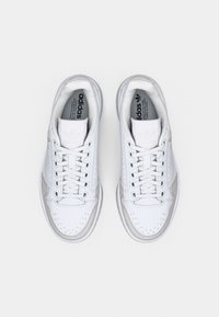 Par hvite Adidas-sneakers med lisser, grå detaljer og merkede innersåler, sett ovenfra på en ensfarget hvit bakgrunn.