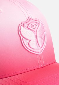 Roze gradient pet met een geborduurd logo van een rozenvlinder. Gemaakt van gladde stof met zichtbare stikseldetails op de rand.