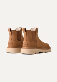 Stivaletti in suede marrone con pannelli elastici laterali, suola tan e cuciture a contrasto; logo UGG sul retro.