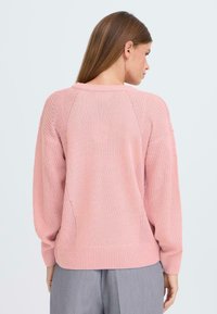 Ljust rosa stickad tröja med avslappnad passform, med en texturerad bakdel, ribbat fåll och neddragna axlar. Mjuk, andningsbar material.