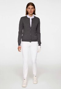 Grå kofta med rund halsringning, knappstängning och långa ärmar, kombinerad med vita byxor och vita sneakers. Slät textur.