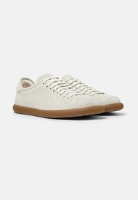 Helles beige, durchlöchertes Sneaker-Modell mit abgerundetem Zehenbereich, Schnürverschluss und brauner Gummisohle. Glatte Textur mit minimalistischem Design.