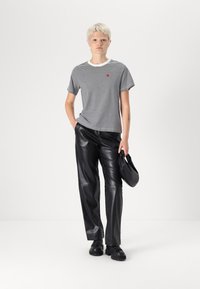 T-shirt rayé noir et blanc avec un col blanc et un cœur rouge brodé, associé à un pantalon en cuir noir et des chaussures noires.