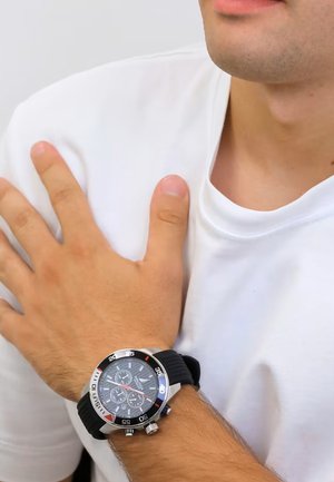 Montre-bracelet noire et argentée avec un cadran rond affichant trois sous-cadrans, bracelet en caoutchouc et accents argentés sur la lunette et la couronne.