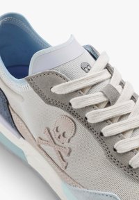 Baskets sportives avec un mélange de suède gris et de mesh, des accents bleu clair et un logo de crâne. Les lacets sont de couleur crème avec une languette rembourrée.