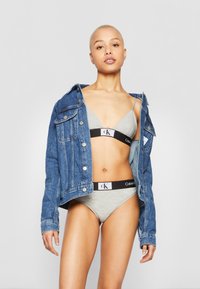 Sivi Calvin Klein bralet i boxerski set, uparen s plavom traper jaknom. Materijali su pamuk i traper, s minimalističkim dizajnom.