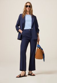 Blazer bleu marine et pantalon taille haute avec un haut bleu clair ; sandales noires à lanières ; sac à main marron avec accent en écharpe bleue.