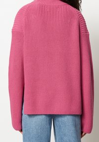 Pull tricoté rose avec un dos texturé, épaules tombantes, col côtelé et coupe décontractée. Associé à un jean bleu clair.