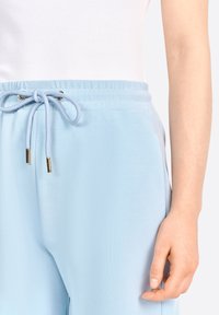 Jogging léger en bleu clair, en tissu lisse, avec une ceinture élastique à cordon de serrage et des accents en métal doré.