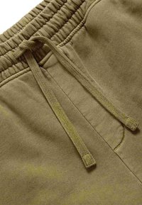 Pantaloni della tuta verde oliva con coulisse e fascia elastica in vita. Texture morbida, con un motivo discreto e dettaglio con tasca laterale.